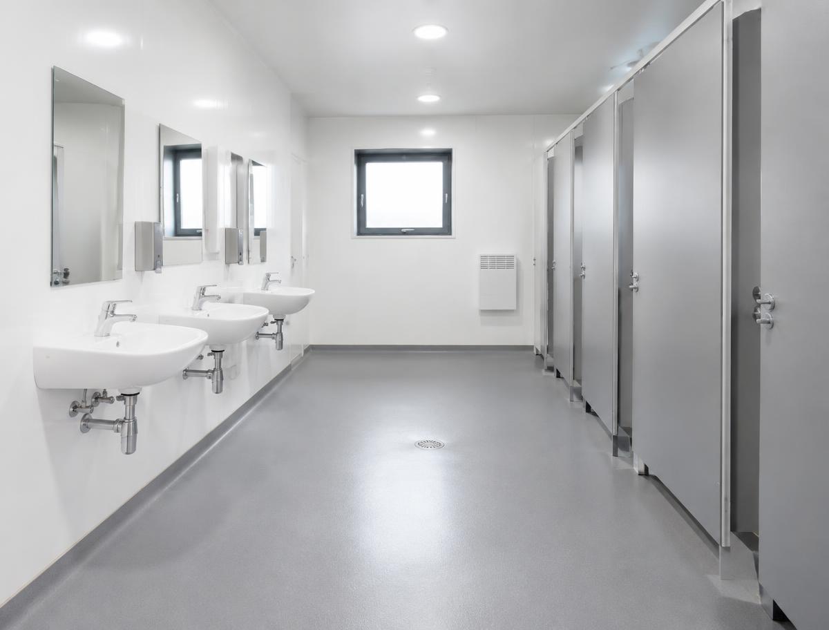 Interior of a modular toilet building with wall-hung basins, cubicles and grey PVC wet-room floor